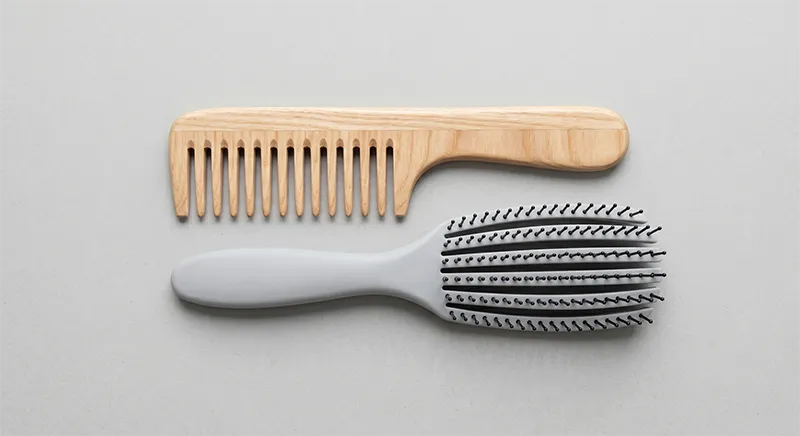Wide-tooth comb and detangling brush laid flat on a neutral surface for fine hair detangling