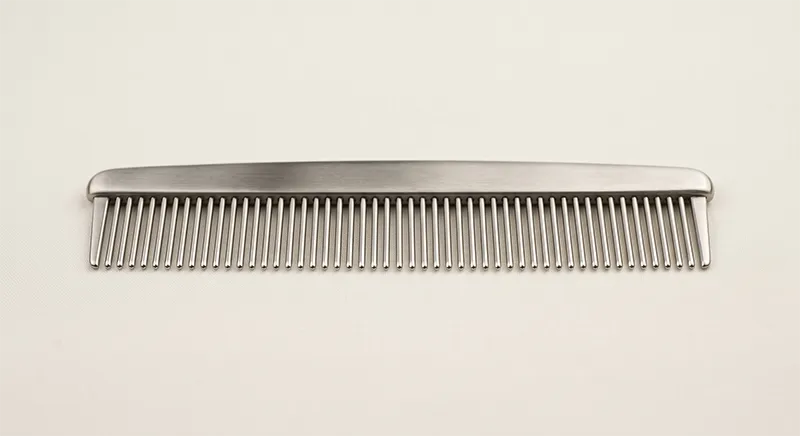 Stainless steel metal comb placed on a neutral surface showing polished teeth and rounded tips