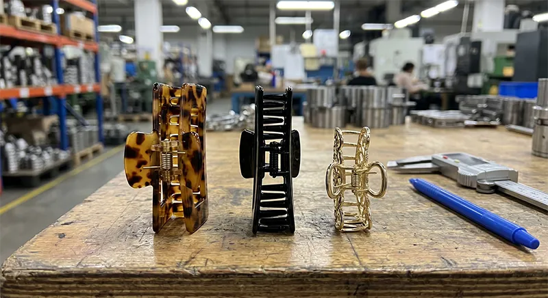 Close-up comparison of cellulose acetate, ABS plastic, and metal zinc alloy claw clips showing material finish and colour differences