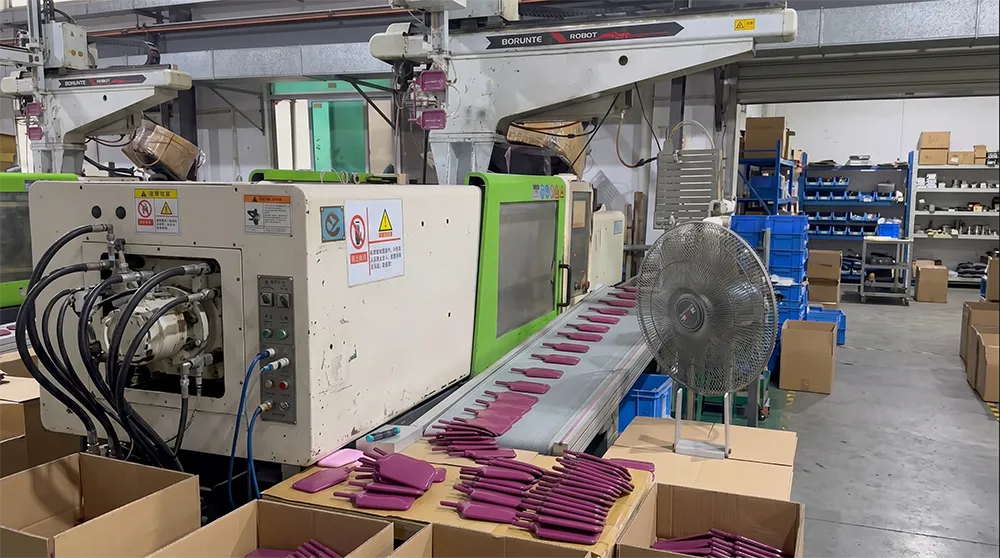 Injection moulding machine producing detangling brush heads with integrated flexible bristles at a factory workstation