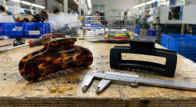 Side by side comparison of acetate hair clip and ABS plastic hair clip on a factory workbench showing visible material quality differences