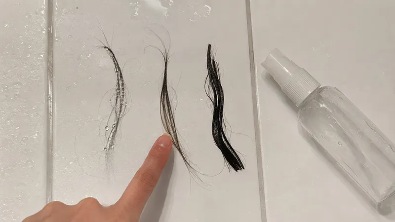 Three hair strands on a white surface showing different water absorption levels after spray test — beading for low porosity, damp for medium, and fully soaked for high porosity