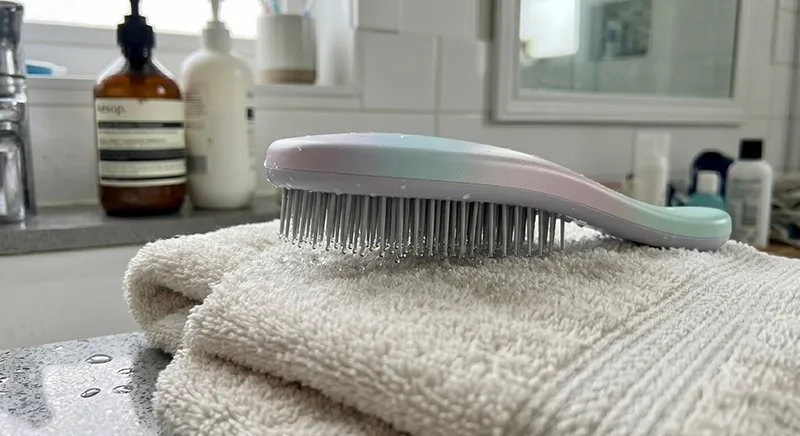 A detangling brush placed bristle-side down on a towel to air dry after cleaning with water droplets visible on the bristles