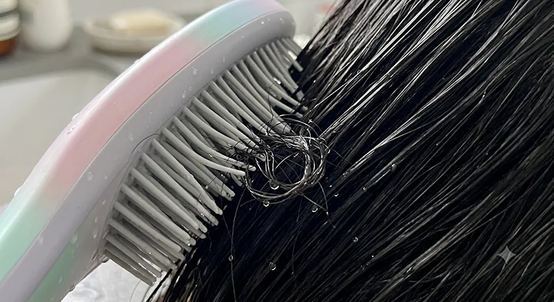 Close-up of a detangling brush bristles bending sideways as they pass through wet tangled hair showing the flex mechanism
