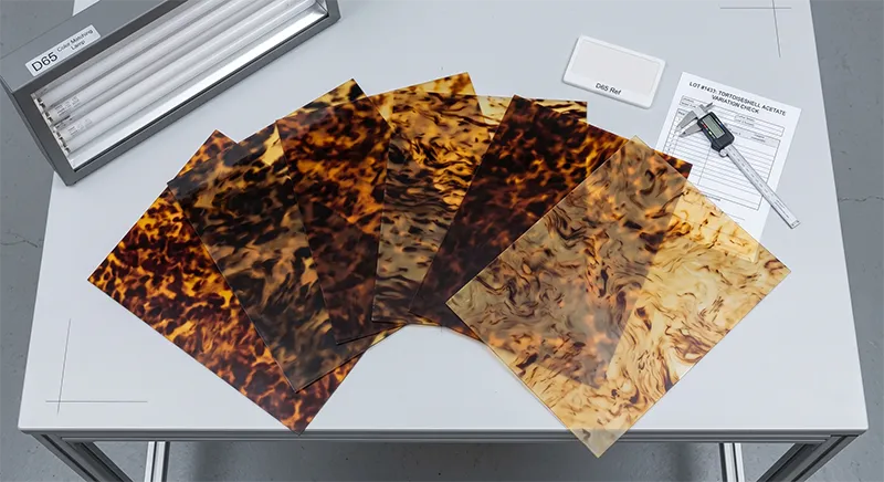 Multiple cellulose acetate sheets in tortoiseshell pattern showing natural colour variation between batches laid out on an inspection table