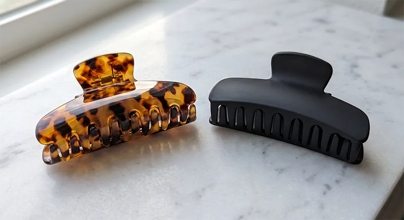 A tortoiseshell cellulose acetate claw clip next to a plain black ABS plastic claw clip showing the difference in colour depth, translucency, and surface finish