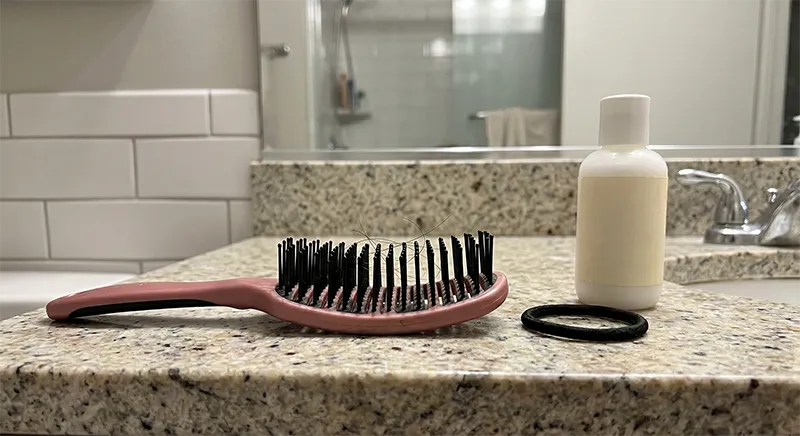 A detangling brush with several broken hair strands caught in the bristles resting on a bathroom counter
