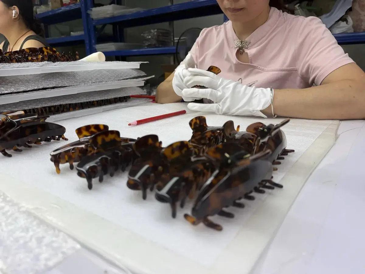 Worker in white gloves inspecting finished tortoiseshell acetate claw clips on a table